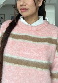 Pull rayé rose et beige avec un col rond, confectionné dans un matériau doux et duveteux, doté d'un col côtelé épais et d'une texture prononcée.