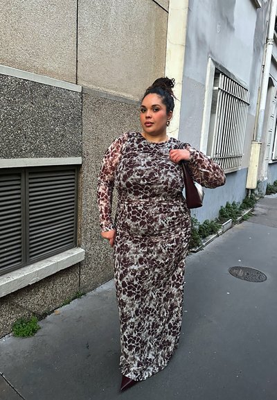 Vestido ajustado de manga larga con un patrón abstracto en marrón y beige, confeccionado con una tela suave, acompañado de un bolso oscuro y zapatos de tacón puntiagudos.