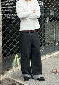 Chemise henley blanche à manches longues avec texture côtelée ; jean en denim noir oversize avec ourlets effilochés ; ceinture en cuir marron ; chaussures noires.