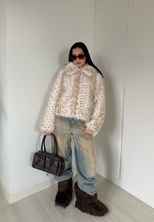 Chaqueta de pelo sintético en crema con manchas marrones, vaqueros sueltos descoloridos, botas marrones peludas y un bolso marrón oscuro. Las gafas de sol completan el look.