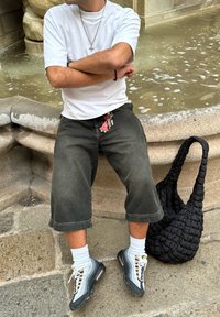 Pantalones cortos de mezclilla gris, camiseta blanca, zapatillas gris con patr�ón, calcetines blancos y un bolso negro texturizado con un diseño trenzado. Llaves visibles en los pantalones cortos.