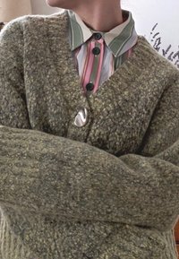 Zielony, teksturowany kardigan z dzianiny z dekoltem w serek i srebrnym guzikiem. Nosi się go na pasiastą koszulę z kołnierzykiem, z różowymi, zielonymi i białymi paskami.