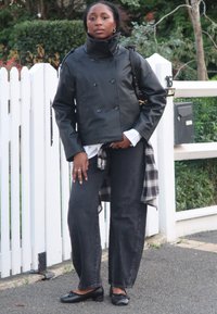 Svart skinnjakke med dobbelspent front og høy krage, brukt over en hvit skjorte, kombinert med mørkegrå vide jeans og svarte ballerinasko.