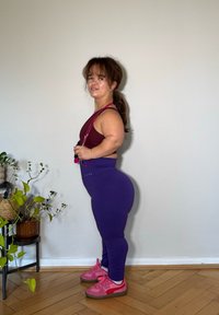 Completo sportivo composto da un top corto borgogna e leggings viola texturizzati. Scarpe rosa, corda per saltare e pianta da interno con un cestino intrecciato.