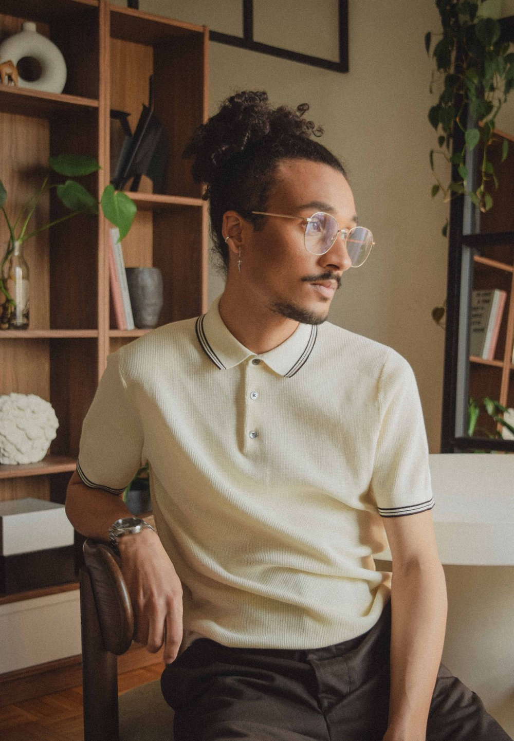 Lichtbeige polo shirt met een gestructureerd patroon, zwarte biezen op de kraag en mouwen, knopen, gecombineerd met donkere broeken en accessoires.