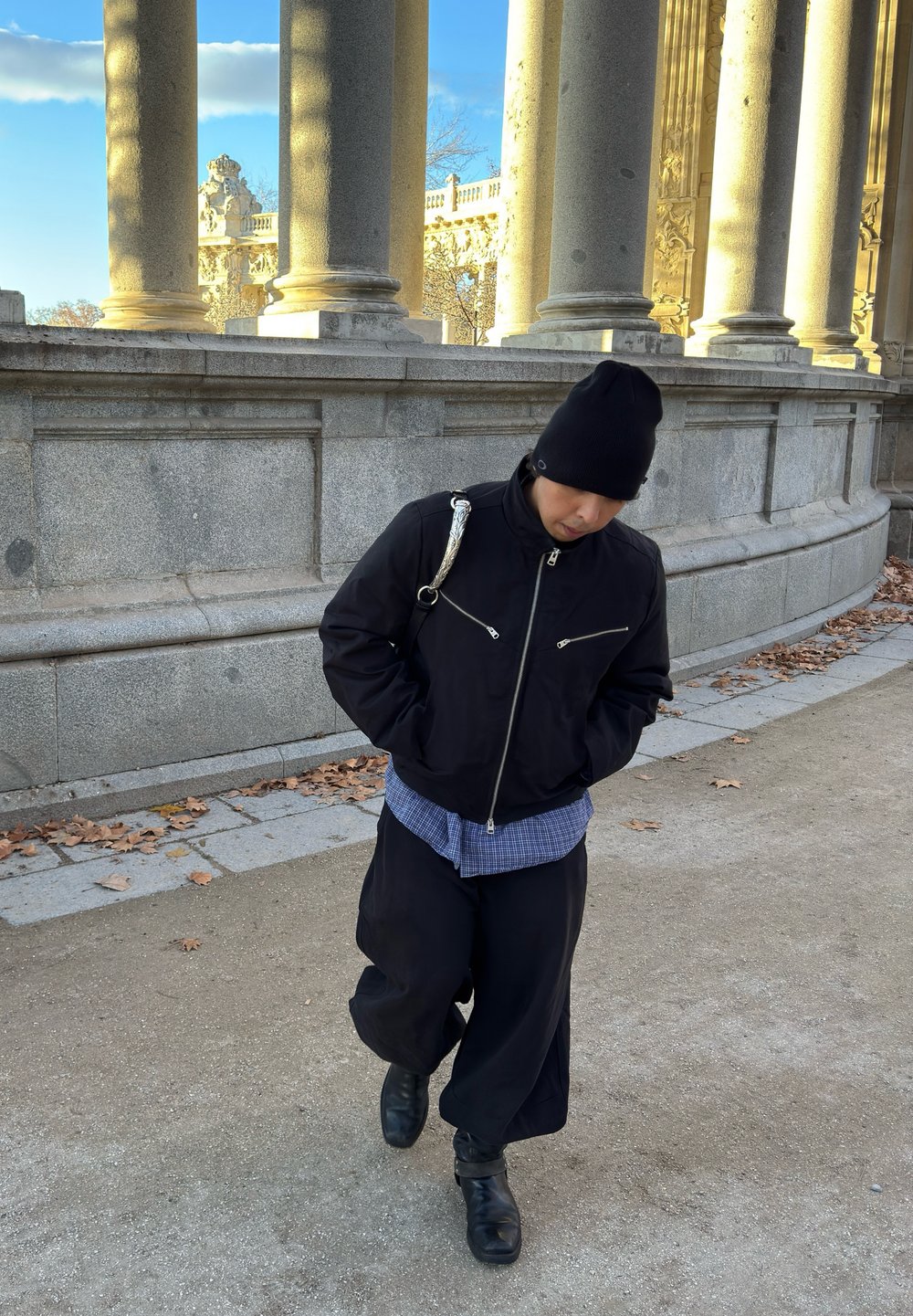 Μαύρο bomber μπουφάν με ασημένιους φερμουάρ, φορεμένο πάνω από ένα μπλε καρό πουκάμισο και χαλαρούς μαύρους παντελόνες. Συνδυασμένο με καπέλο beanie και μαύρα μποτάκια.