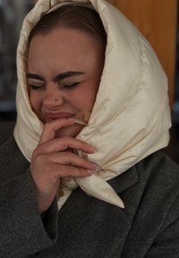 Krém színű selyem szatén, túlméretezett sál, amely a fej köré van tekerve, ellentétben egy szürke kabáttal. Simogató tapintású, és egy nagy csomó díszíti a nyaki résznél.