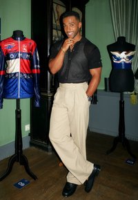 Svart kortärmad skjorta med vertikala ränder, beige byxor och svarta skor. Visar en cykeltröja i röd, blå och vit på en docka.