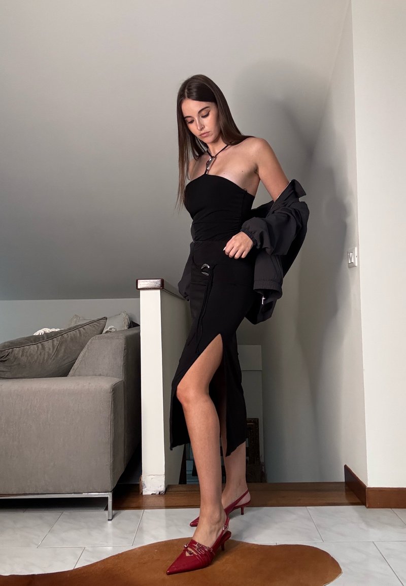 Svart strapless klänning med rynkning, sidofrak och svarta detaljer. Bärs med en grå jacka och röda spetsiga klackskor. Släta texturer genom hela outfiten.
