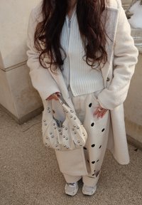 Γυναίκα που φοράει εκρού παλτό, ανοιχτό μπλε ριμπ ζακέτα με φερμουάρ, εκρού παντελόνι με μαύρες πουά, λευκά αθλητικά παπούτσια και κρατάει εκρού τσάντα με καρφιά.