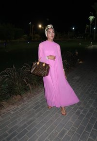 Lang rosa kjole med gjennomsiktige ermer, paret med en brun Louis Vuitton veske. Kveldssetting med grøntområder og dempet belysning i bakgrunnen.