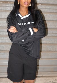 Jersey desportivo preto da Nike com detalhes brancos, apresentando um design com colarinho. Combinado com calções pretos, que exibem um ajuste descontraído e uma textura suave.
