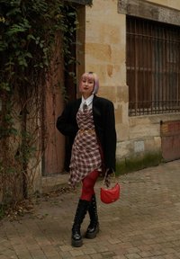 Lagdelte tøj bestående af en brun ternet kjole, en oversized sort blazer, røde strømpebukser, sorte combat støvler og en lille rød håndtaske.