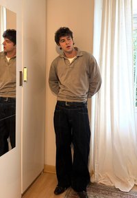 Pull-over en polaire gris avec col, associé à un jean en denim foncé. La surface réfléchissante d'un meuble est visible à côté d'un rideau.