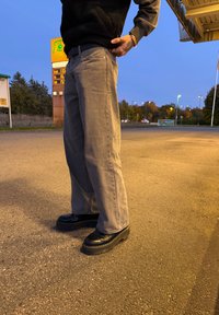 Pantaloni largi gri, pantofi cu platformă negri cu talpă groasă, cusături vizibile, purtați într-un cadru exterior în timpul amurgului.
