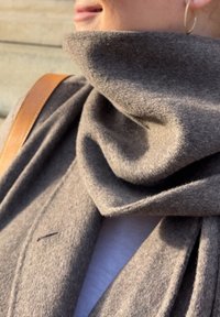 Grå ullscarf med mjuk textur, hängande i en loop runt halsen, med en subtil vikning och en liten dekorativ söm.