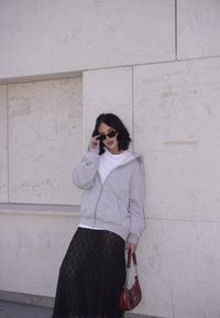 Grey zip-up hoodie, white t-shirt, black lace maxi skirt, and red handbag. The model is wearing black sunglasses and is standing against a light-coloured wall.