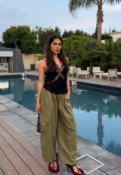 Top sin mangas negro con encaje, combinado con pantalones cargo verdes olivo holgados. Tacones de fucsia con acentos de piel completan el atuendo. Ambiente junto a la piscina.