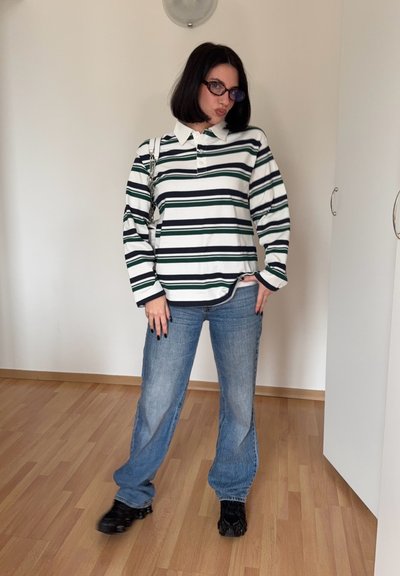 Polo de manga larga a rayas en blanco, azul marino y verde, combinado con unos vaqueros anchos azules y zapatos negros. Gafas reflectantes y cadena visible en el strap.