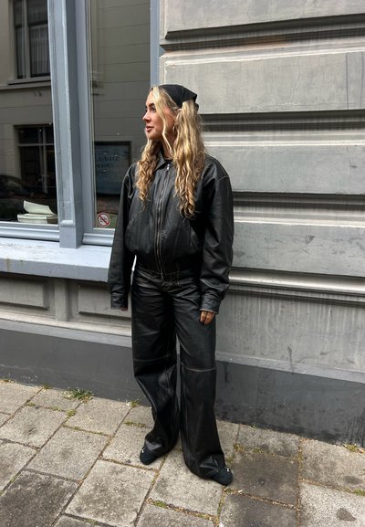 Conjunto de cuero negro que incluye una chaqueta de gran tamaño con cremallera y pantalones de pierna ancha. Textura suave, detalles mínimos y una silueta relajada.
