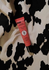 Nudestix Nudescreen Blush Tint SPF 30 i en pink tube med sort hætte, placeret på et hvidt og sort ko-print stof.