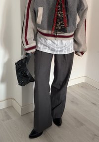 Casaco bomber cinza de malha com riscas vermelhas e pretas, top branco texturizado, Calças cinza de boca de sino e uma mala preta com padrão. Botas pretas de bico fino.