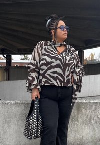 Blouse à motifs zèbre noir et blanc avec manches à volants, associée à un jean noir taille haute et un sac à main noir clouté.