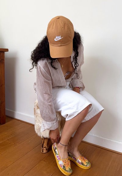 Zapatos slip-on florales multicolores con una suela amarilla trenzada; combinados con pantalones anchos blancos y una camisa de botón a rayas.