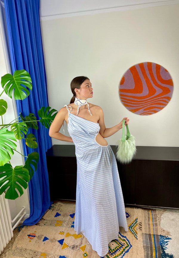 Blauwe en witte gestreepte maxidress met een asymmetrische uitsnede, aangevuld met een fluffy mintgroene handtas en een patroonwandhanger.