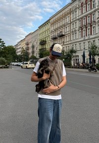 Jongere persoon in casual kleding die een kleine zwart-bruin hond vasthoudt op een stadsstraat met historische gebouwen en voetgangers buiten.