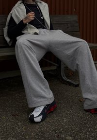 Šedé tepláky vyrobené z měkké látky s pohodlným střihem, doplněné o bílé a námořnické tenisky Nike s červenými akcenty.