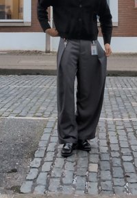 Šedé volné kalhoty s pregamy, spárované s černým kardigánem na knoflíky. Na sobě má černé boty, které mají viditelný klip na klíče.