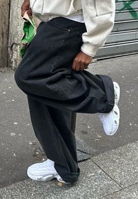 Černé široké džíny s uvolněným střihem, doplněné o bílé sportovní tenisky s výraznými kulatými detaily a texturovanými vzory.