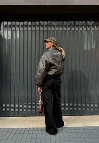 Schwarze Leder-Bomberjacke mit gerippten Bündchen und besticktem Rücken, kombiniert mit schwarzen Jeans, einer Leopard-Print-Mütze und einer braunen Tasche.