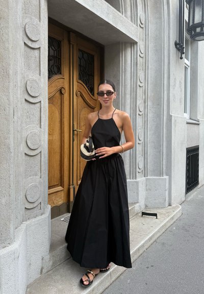 Vestido negro con cuello halter y falda fluida, combinado con un bolso texturizado en negro y crema. Los accesorios incluyen unas pequeñas gafas de sol negras.