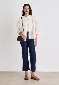 Lightweight, striped cream blouse tucked into dark blue flared jeans. Brown handbag and brown moccasin-style shoes with hardware detailing.