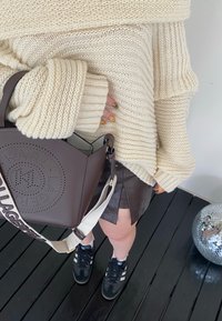Jersey de punto crema con puños enrollados, bolso marrón perforado, zapatillas negras y una falda de cuero oscura con detalle de abertura.