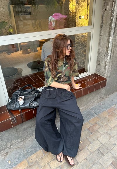 Camisa de patrón de camuflaje de manga corta, combinada con pantalones holgados negros. Un bolso negro con un llavero de juguete está cerca.