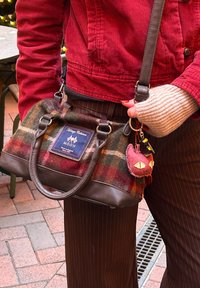 Sac à main en cuir marron avec un motif à carreaux multicolores, comprenant une étiquette bleue et un porte-clés en peluche rose avec des yeux ressemblant à ceux d'un chat.