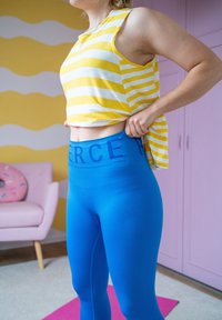 Κίτρινη και λευκή ριγέ αμάνικη μπλούζα, συνδυασμένη με στενά μπλε κολάν που διαθέτει έντονη ζώνη με την επιγραφή "FIERCE".