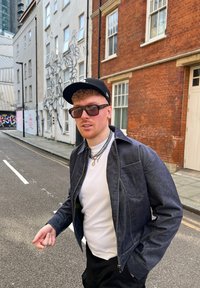 Τζάκετ από τζιν σε σκούρο μπλε χρώμα, με λευκό μπλουζάκι από κάτω, στρωμένο με ασημένιες αλυσίδες. Το μαύρο καπέλο και τα υπερμεγέθη γυαλιά ηλίου ολοκληρώνουν την εμφάνιση.