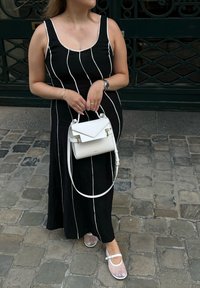 Μαύρο φόρεμα με ρίγες και λευκές γραμμές, συνδυασμένο με διαφανές σανδάλι και μικρή λευκή τσάντα. Απαλή υφή, μεσαίου μήκους σχέδιο και ρυθμιζόμενες τιράντες.