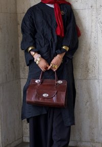 Borsa a mano in pelle marrone con forma strutturata, hardware argentato e due manici superiori, abbinata a un indumento in tessuto a righe nere e una sciarpa rossa.