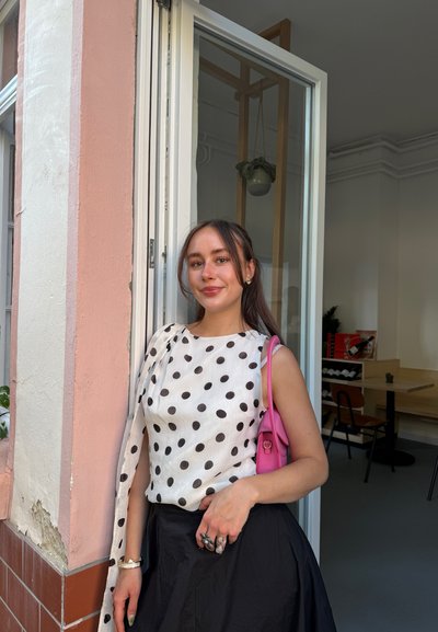 Blusa de lunares en blanco y negro, con detalle de hombro ajustado, combinada con una falda negra. Bolso rosa con acentos plateados, en interior con decoración mínima.