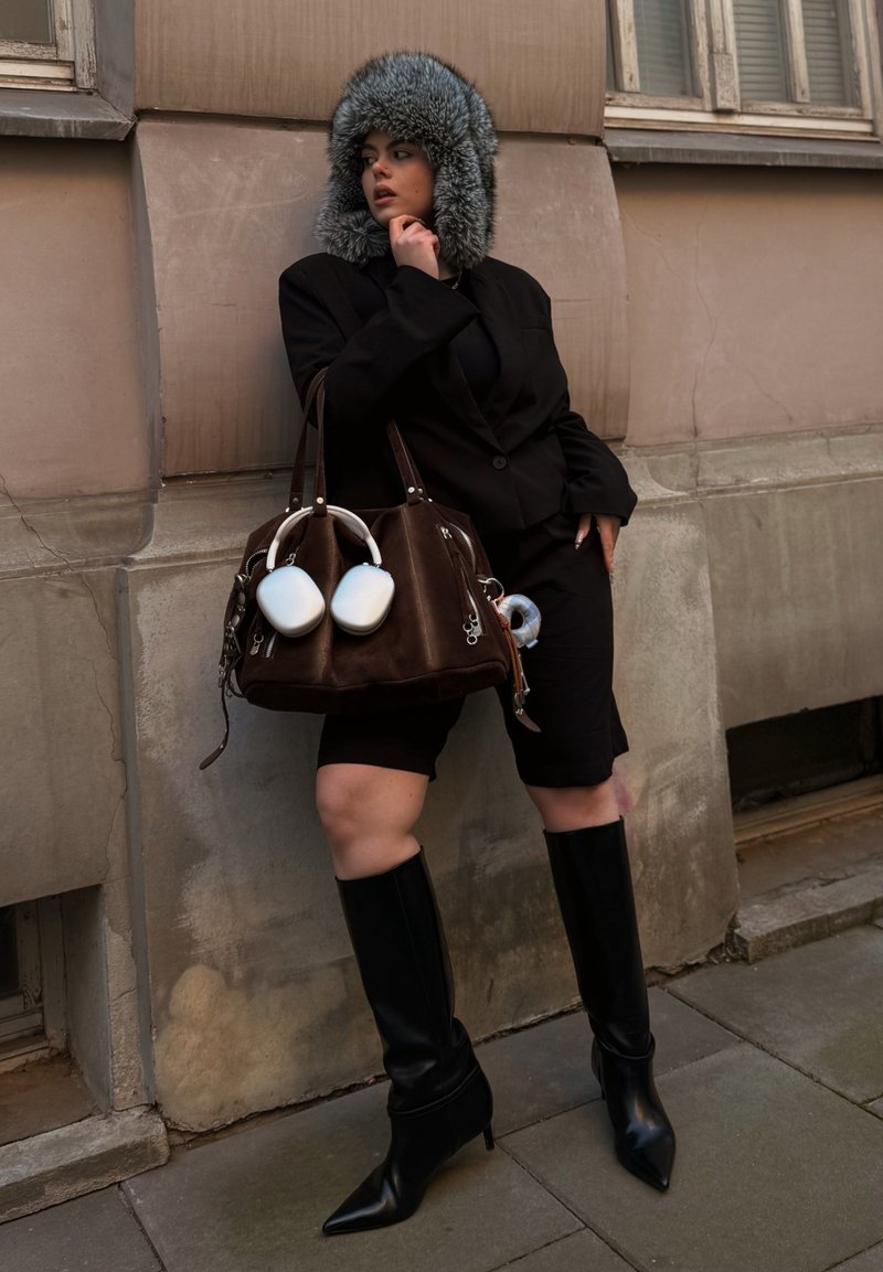 Black blazer over a black top and shorts, paired with knee-high black stiletto boots. Brown bag with white accents and fur hat.