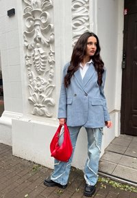 Ανοιχτού μπλε σακάκι με λευκές ρίγες και διπλά κουμπιά, λευκό πουκάμισο από κάτω, ξεθωριασμένα ανοιχτού μπλε τζιν και μια ζωντανή κόκκινη τσάντα χειρός. Μαύρες πλατφόρμες.