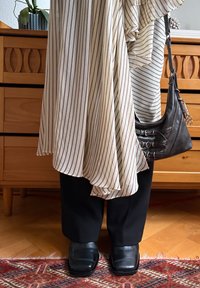 O tunică rayată bej și bordeaux purtată peste pantaloni negri, asociată cu pantofi negri din piele și o geantă mică din piele neagră cu cusături decorative.
