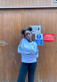 Hvid langærmet top med lodrette striber og sorte detaljer, kombineret med sorte bukser. Baggrunden består af træplanker og skilte.