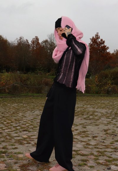 Camisa negra de corte holgado con diseño de rayas transparentes, bufanda rosa y pantalones anchos negros. Zapatillas de deporte en rosa claro completan el conjunto.