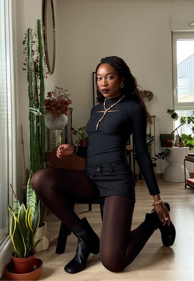 Top negro de manga larga con un detalle recortado, combinado con una falda negra, medias negras transparentes y botines negros. Accesorios de joyería dorada.